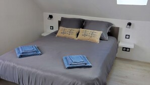 Une chambre à coucher avec un lit, deux oreillers, une table de chevet, une lampe fixée au mur et un puits de lumière.