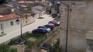 Une rue étroite bordée de bâtiments historiques en pierre, une rangée de voitures garées et, au loin, le clocher d’une église.