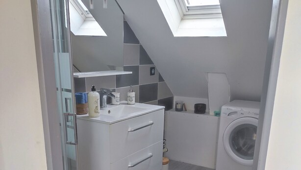 Une salle de bain moderne avec un puits de lumière, un lave-linge et un meuble-lavabo blanc.