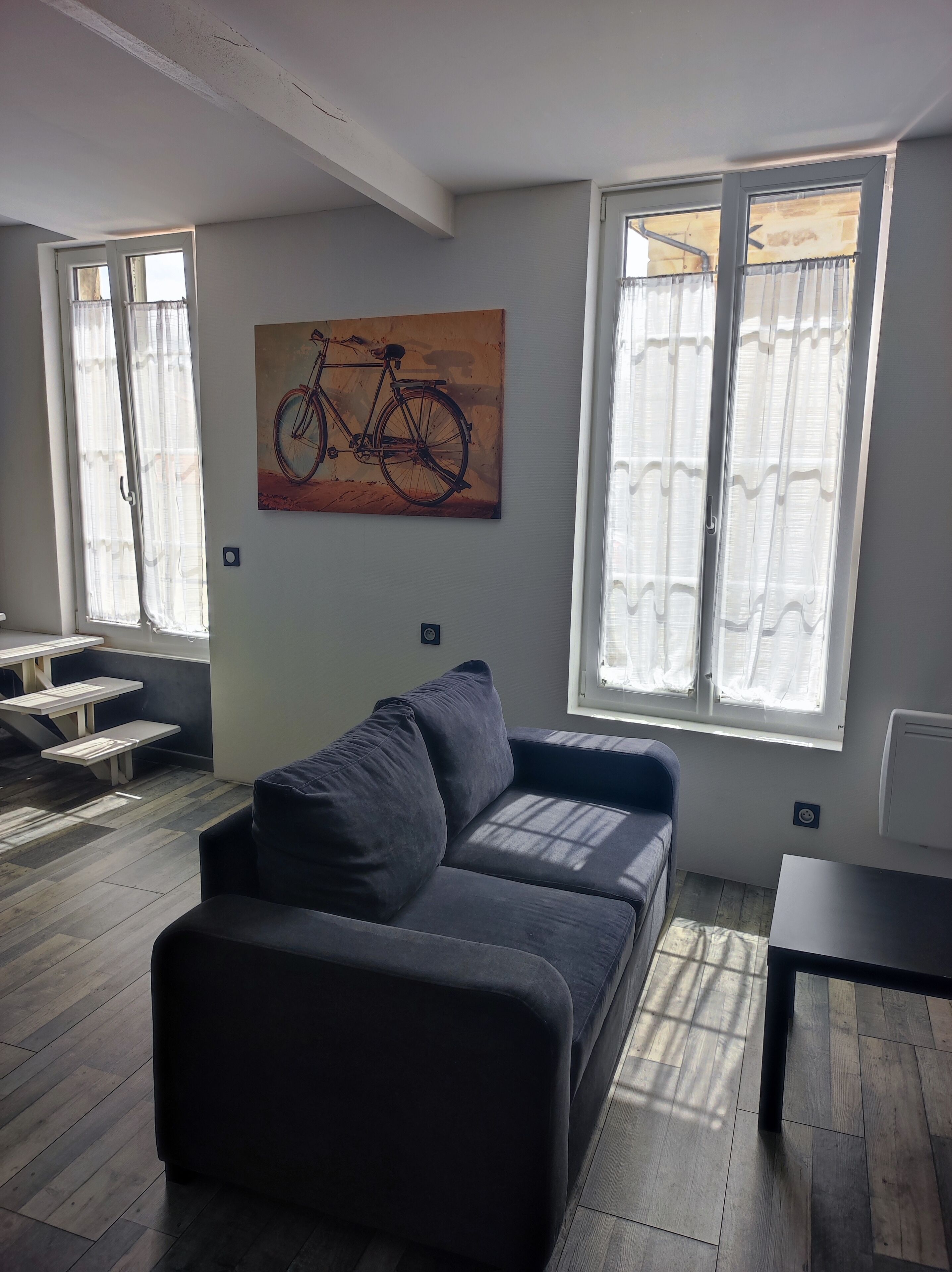 Ett modernt vardagsrum med en grå soffa, en tavla som föreställer en cykel och stora fönster med gardiner.