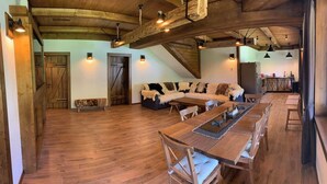 A spacious room with a wooden floor, a large sofa, a dining table with chairs, and a staircase leading to another level. - Avalanche (Zarnesti)