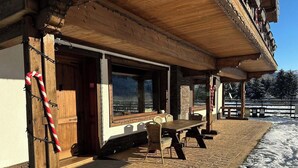 A wooden outdoor seating area with a table and chairs, a view through a window, and a snow-covered ground. - Avalanche (Zarnesti)
