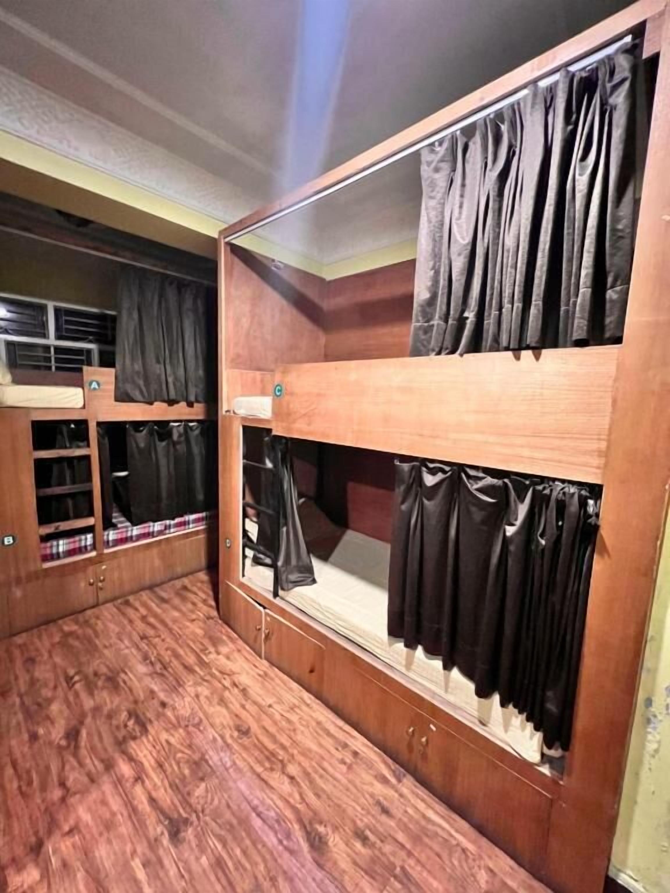 A bunk bed room with wooden walls and a large mirror. There are two bunk beds, each with a curtain.