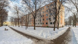 Un sendero cubierto de nieve con árboles y un edificio de varios pisos al fondo.