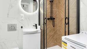 Un baño moderno con ducha de vidrio, lavamanos blanco y espejo con marco circular.