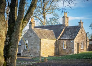A stone building with a sloped roof and chimneys, surrounded by trees. - Library Cottage near Gorebridge (Gorebridge)