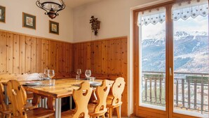 Ein Esszimmer aus Holz mit einem großen Tisch und Stühlen, einer Wanduhr und Blick auf schneebedeckte Berge durch ein großes Fenster.