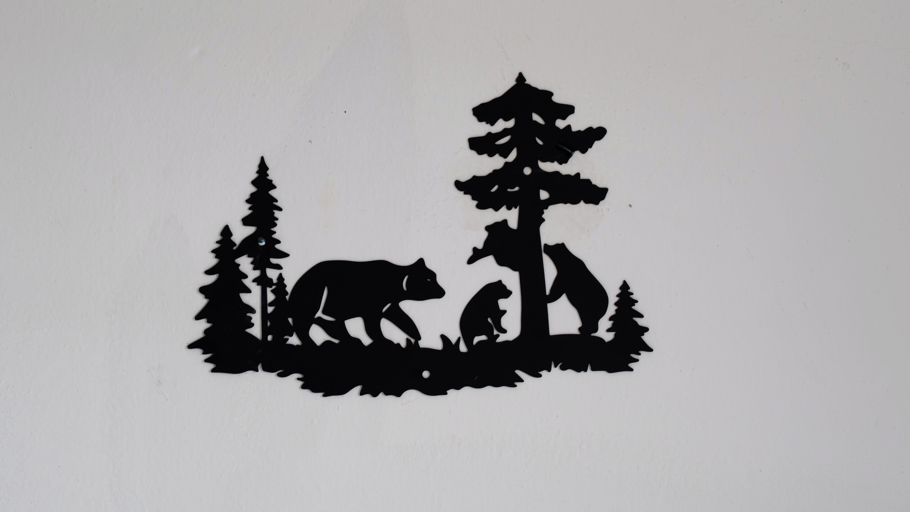 A black silhouette of a bear, a dog, and a person standing among trees on a white background.