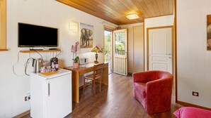 Habitación con techo de madera, un televisor de pantalla plana montado en la pared, un escritorio con una silla, un sillón rojo y una puerta que da al exterior.