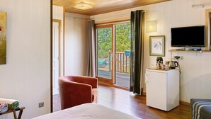 Una habitación con una cama, un sillón rojo, un refrigerador blanco pequeño, un televisor y una puerta corrediza de vidrio a una terraza.