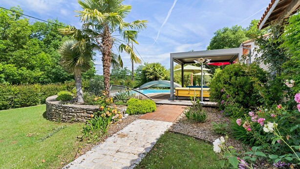 Un sendero en el jardín que conduce a una zona de estar techada, con una piscina al fondo.