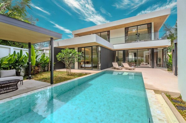 Een modern huis met een zwembad, een overdekt terras en een grote glazen deur die leidt naar een woonruimte.