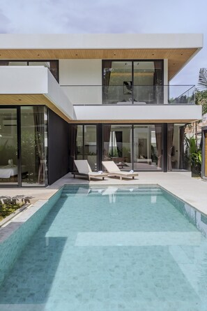 Een modern herenhuis met zwembad, glazen deuren en een balkon met lounge stoelen.