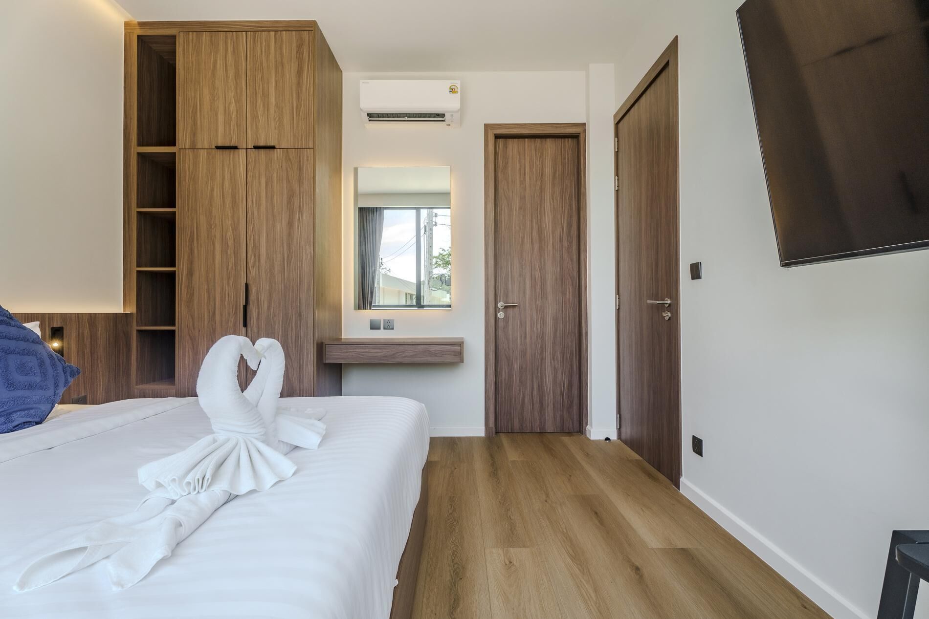 A hotel room with a bed, a wardrobe, a mirror, a television, and a small desk.