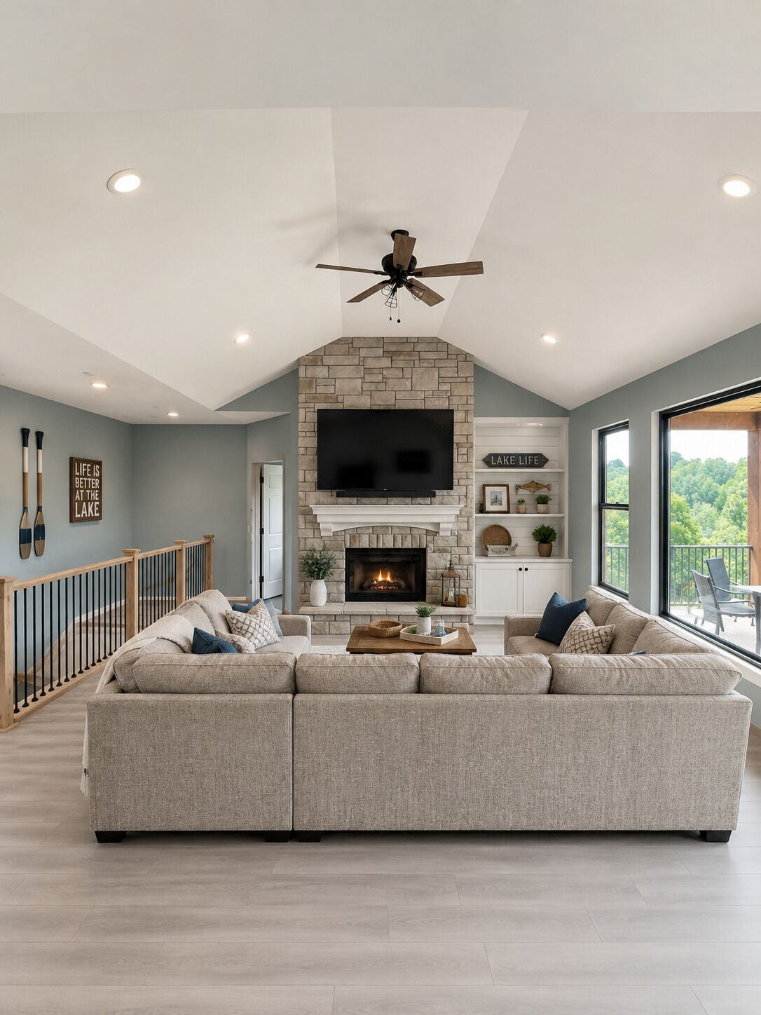 A modern living room with a stone fireplace, a large flat-screen TV, and a ceiling fan.