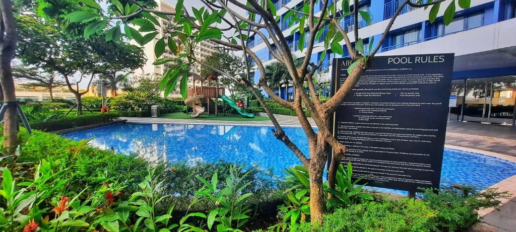 A swimming pool with a sign detailing pool rules, surrounded by greenery and a building in the background.
