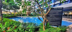 Una piscina con un cartel que detalla las normas de la piscina, rodeada de vegetación y un edificio al fondo.