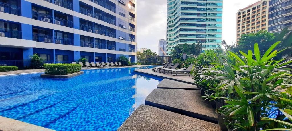 A swimming pool with lounge chairs, surrounded by greenery and modern buildings.