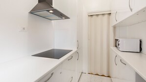 Una cocina estrecha con armarios blancos, una encimera negra y un microondas.
