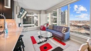 Ein modernes Wohnzimmer mit einer Couch, einem Fernseher und einem großen Fenster mit Blick auf die Stadt.
