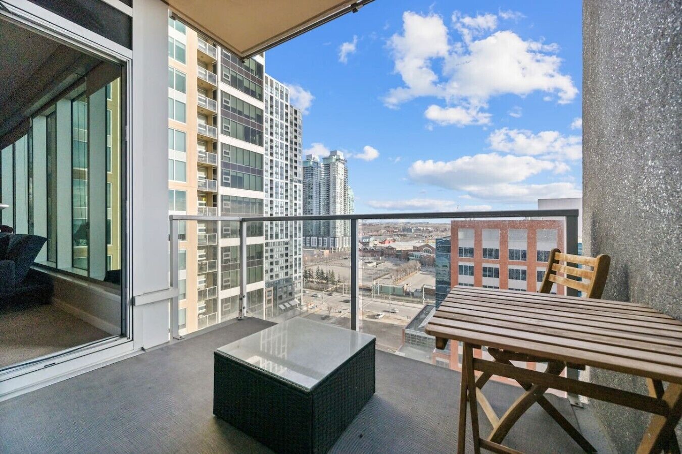Uma varanda com mesa e cadeiras, um painel de vidro e vista para edifícios altos.