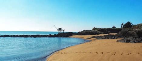 A beach with a rocky shoreline, a lifeguard tower, and footprints in the sand.