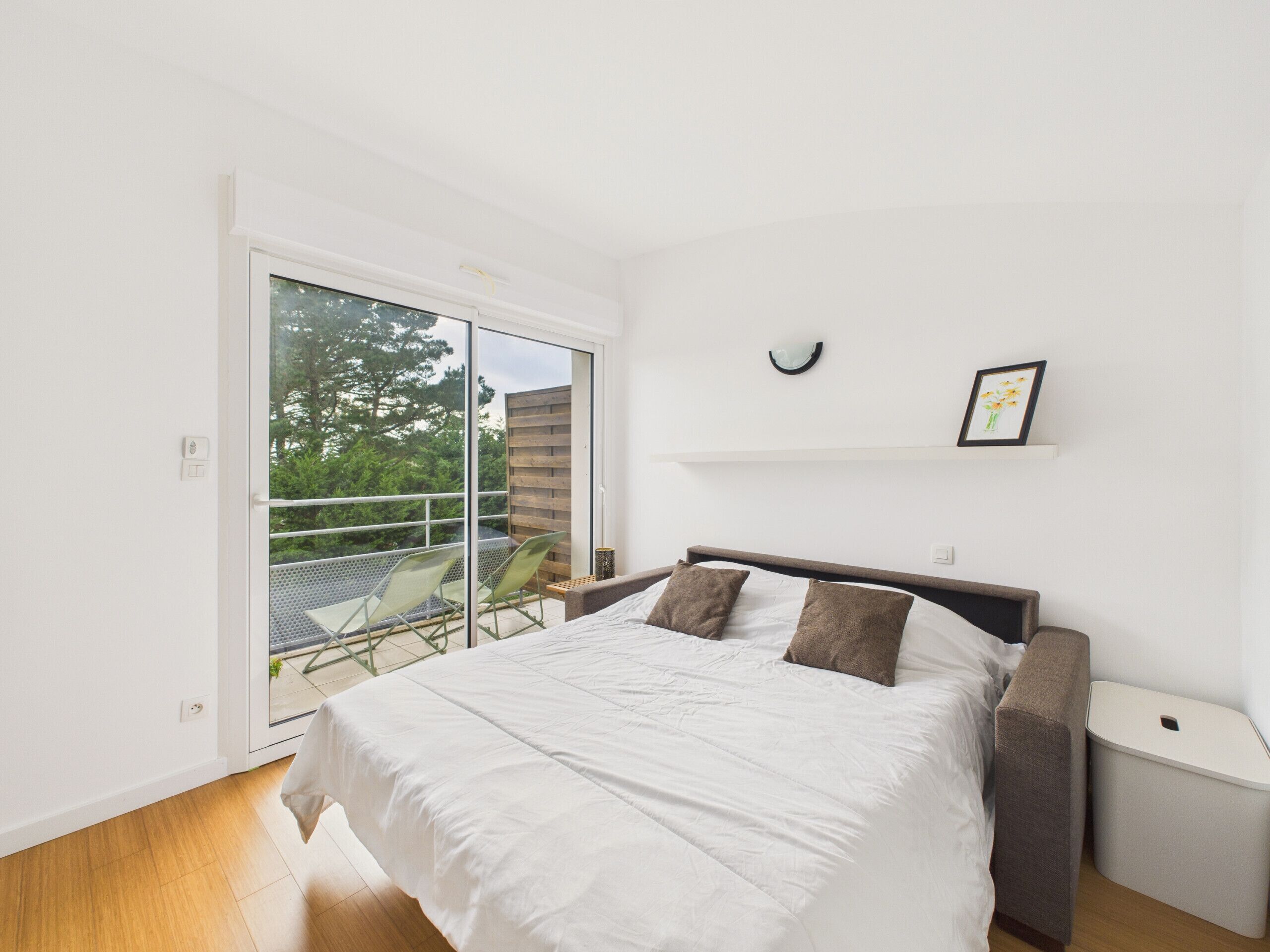 A bedroom with a bed, a nightstand, a small table, a chair, and a sliding glass door leading to a balcony.