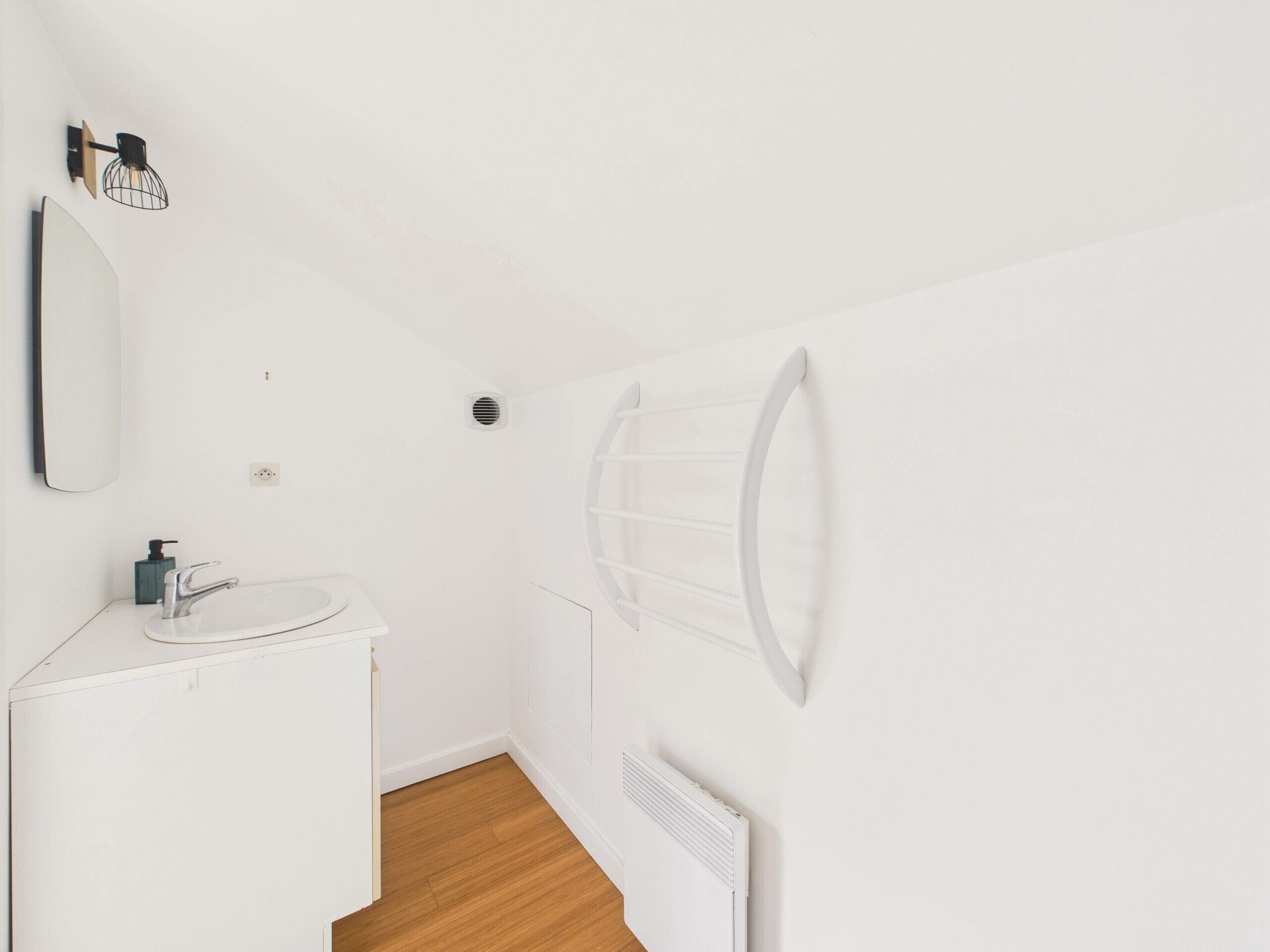 A white bathroom with a sink, mirror, and a wall-mounted towel rack.