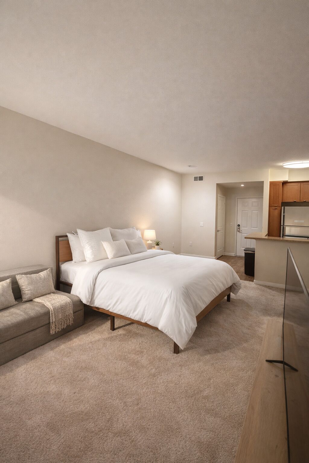 Quarto com cama, mesa de cabeceira, sofá e piso de madeira.
