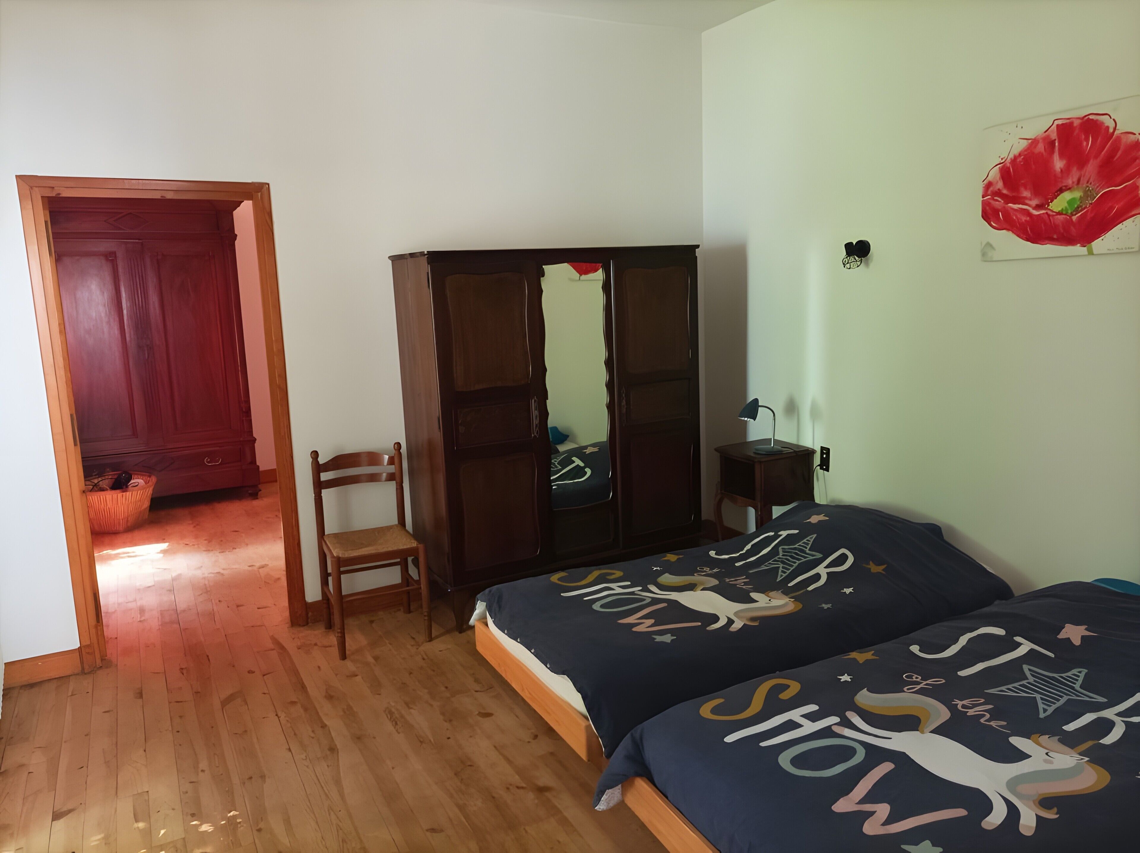 Ein Schlafzimmer mit Holzboden, einem Kleiderschrank, einem Sessel, einem Bett mit Sternenmuster und einem Gemälde einer roten Blume an der Wand.