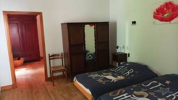 Ein Schlafzimmer mit Holzboden, einem Kleiderschrank, einem Sessel, einem Bett mit Sternenmuster und einem Gemälde einer roten Blume an der Wand.