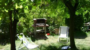 Un jardin avec un barbecue, deux chaises de jardin et un arbre.