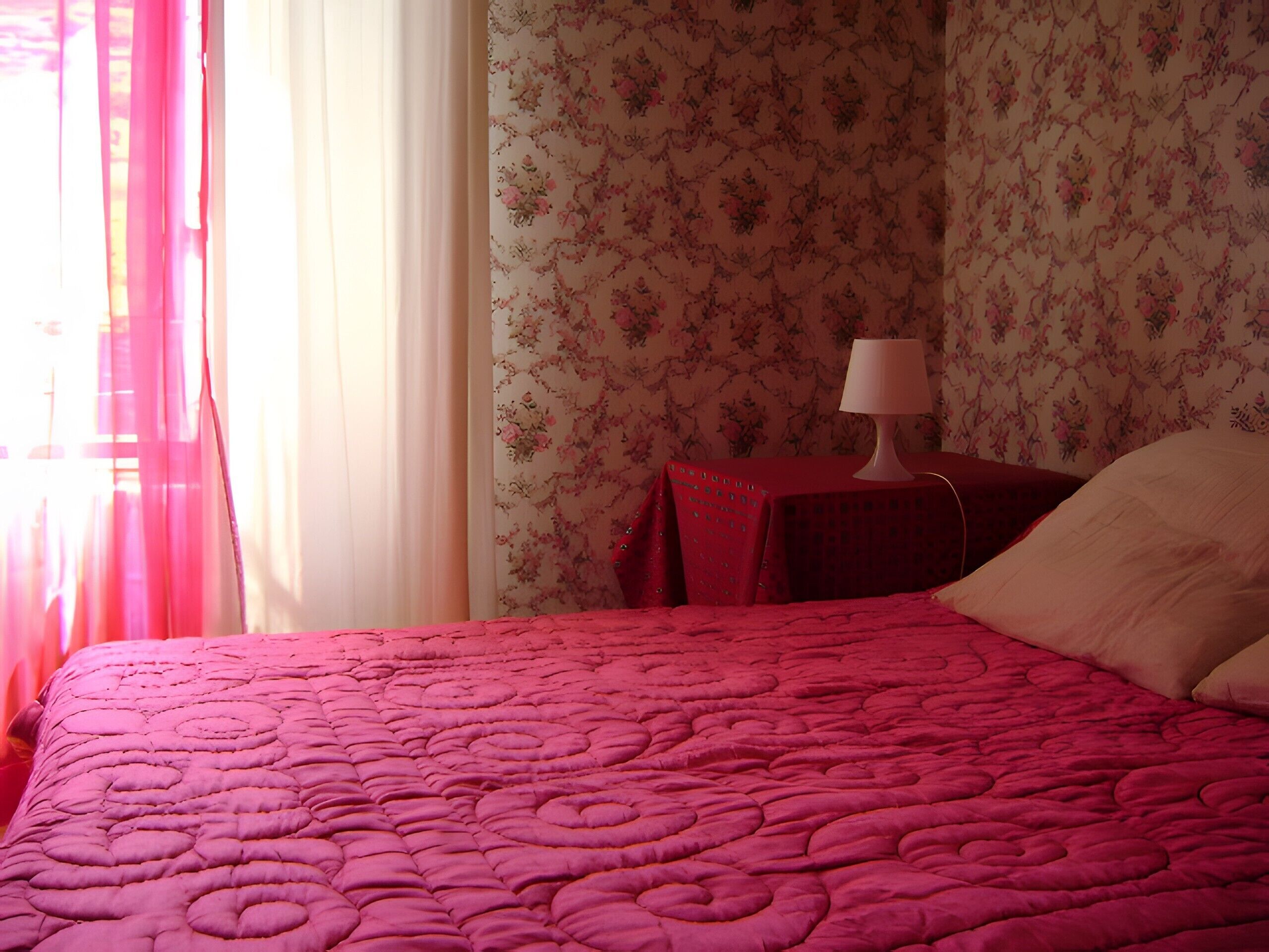 A room with a bed, a nightstand with a lamp, and floral wallpaper.