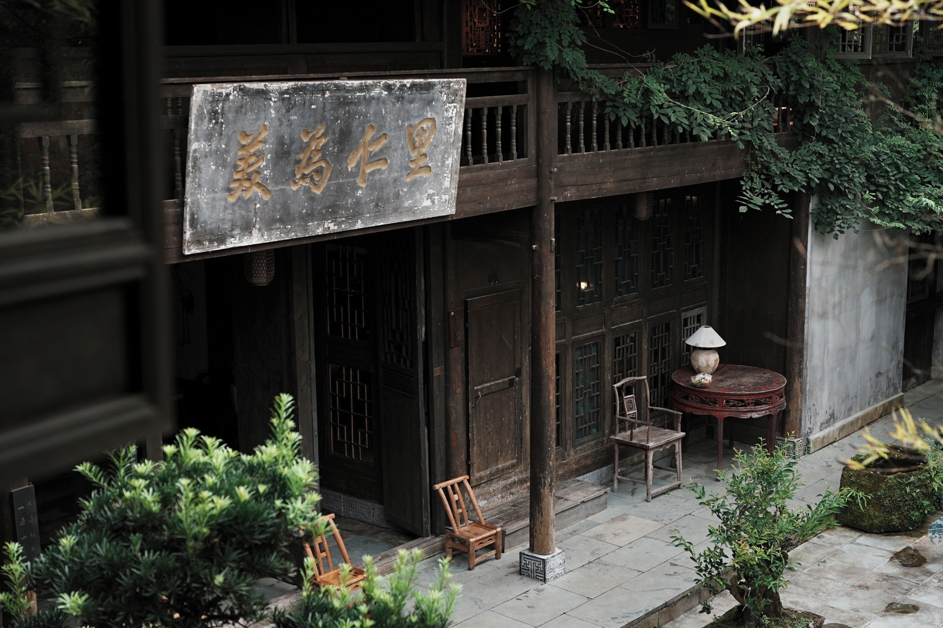 A traditional building with a signboard, wooden doors, and a small outdoor seating area with chairs and a table.