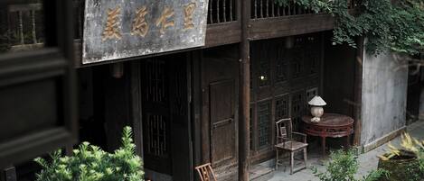 A traditional building with a signboard, wooden doors, and a small outdoor seating area with chairs and a table.