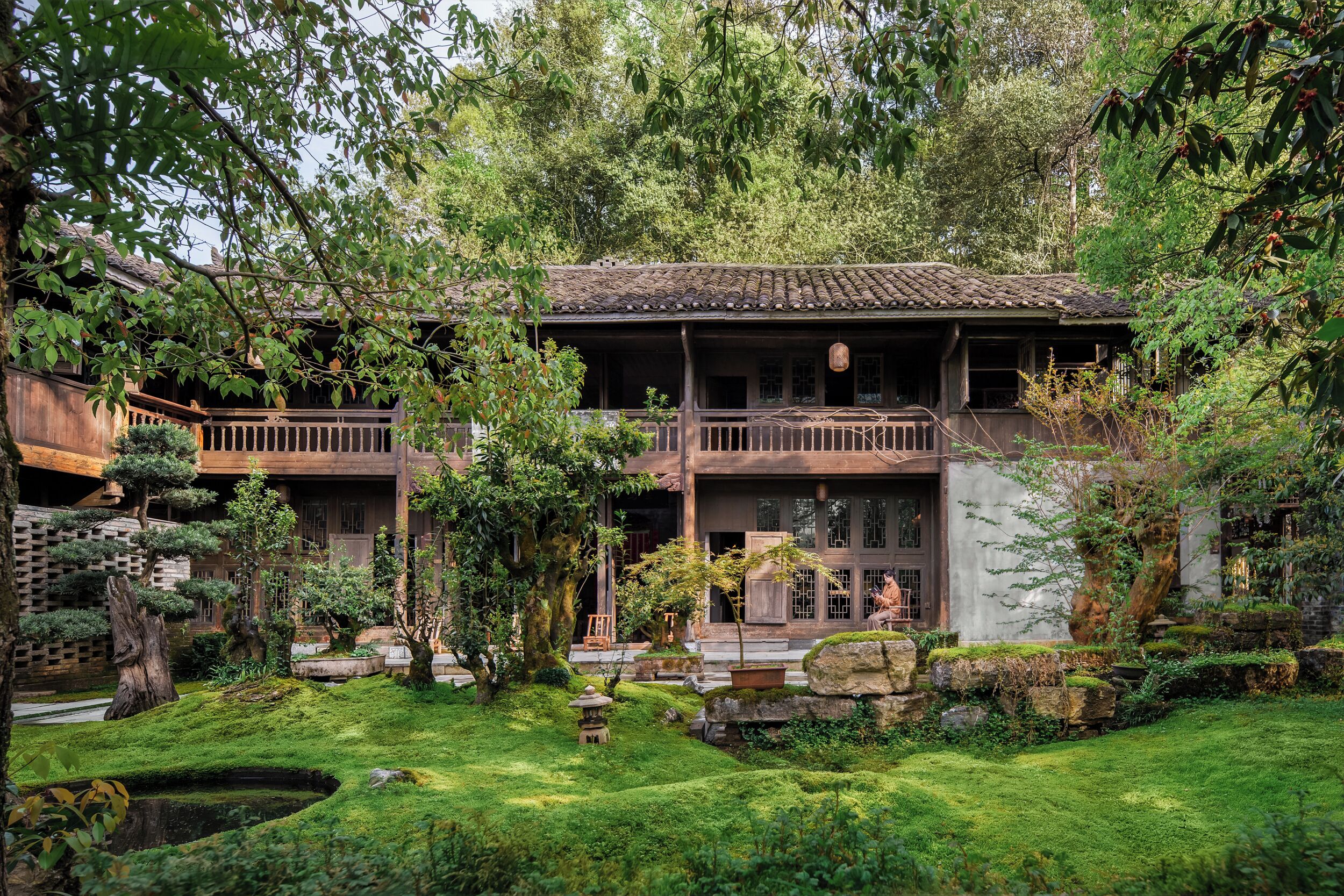 A traditional Japanese-style building with a wooden exterior, multiple floors, and a garden with a pond and various plants.