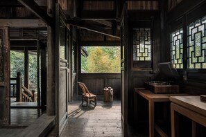 A wooden interior with a wooden chair, a table, and a window with a view of trees. - Fanjingshan Ansu Homestay (Tongren)