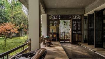 Un porche de madera tradicional con vistas a un jardín, un banco de madera y una mesa con un reloj.