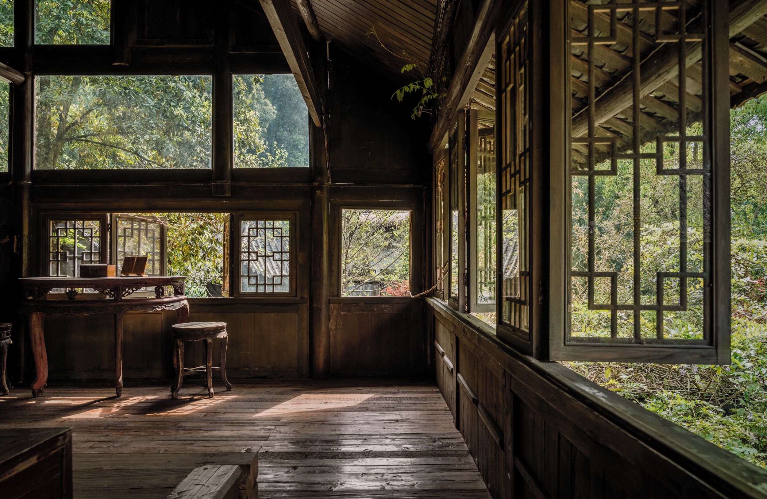 A traditional wooden room with large windows, a wooden table, and a bench.
