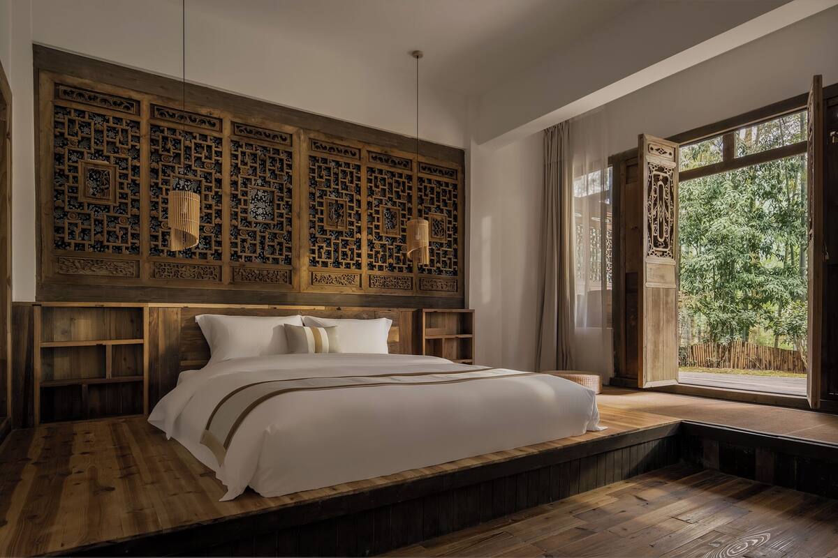 Ein Schlafzimmer mit einem großen Bett, einem Holz-Kopfteil, eingebauten Regalen und einem Fenster mit Blick auf Grünflächen.