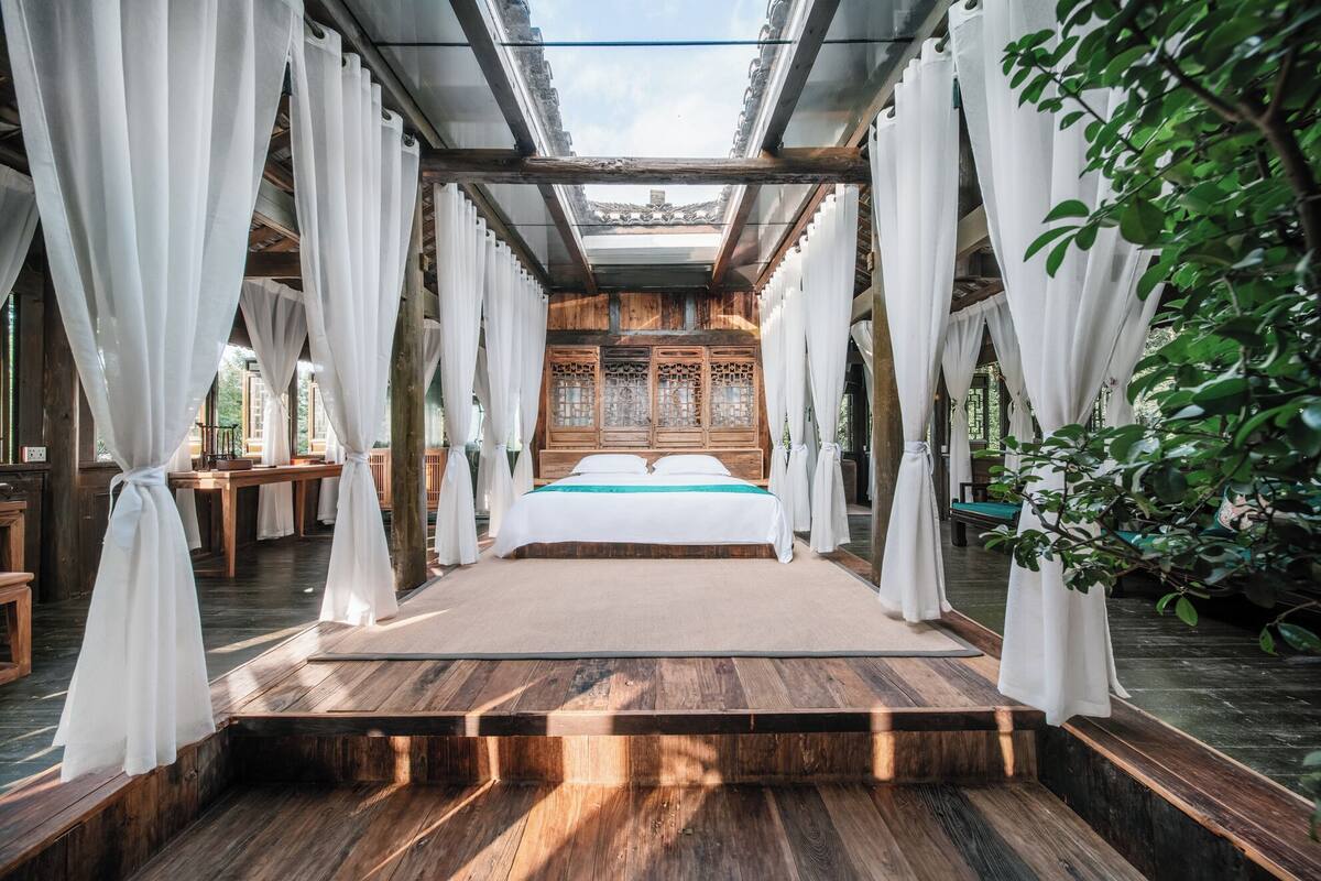 Ein traditionell eingerichtetes Zimmer mit einem Holzbett, weißen Vorhängen und Blick auf ein traditionelles Gebäude.