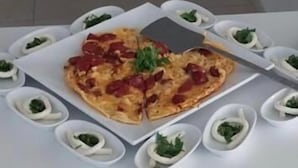 Une table à manger avec une pizza et de petits bols garnis d’herbes vertes.