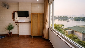 Ein Hotelzimmer mit Holzboden, einem an der Wand montierten Flachbildfernseher, einem Fenster mit Blick auf einen Fluss und eine Stadtlandschaft sowie einem hölzernen Kleiderschrank.
