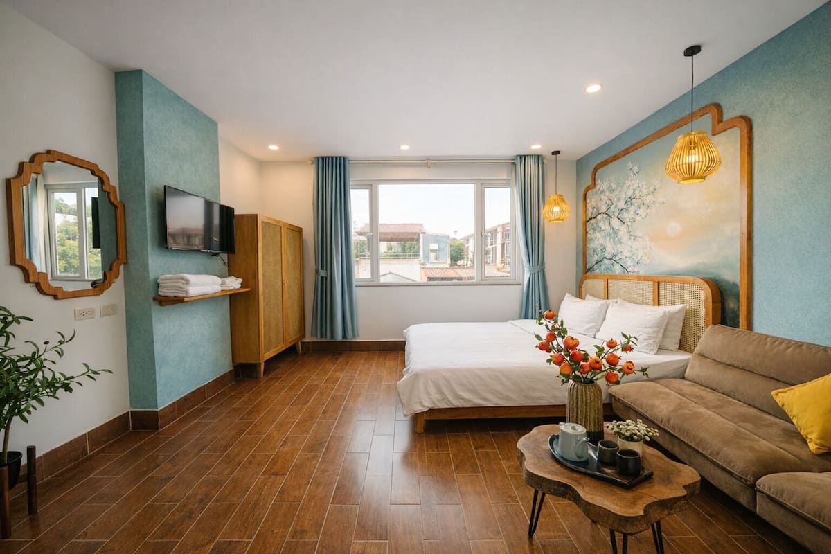 Une chambre d’hôtel avec un lit, un canapé, une télévision, une armoire en bois, une fenêtre avec des rideaux et un tableau au mur.