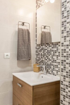 A bathroom with a white sink, wooden cabinet, and a tiled wall with a mosaic pattern. - Splendid apartment next to Gran Vía (Madrid)