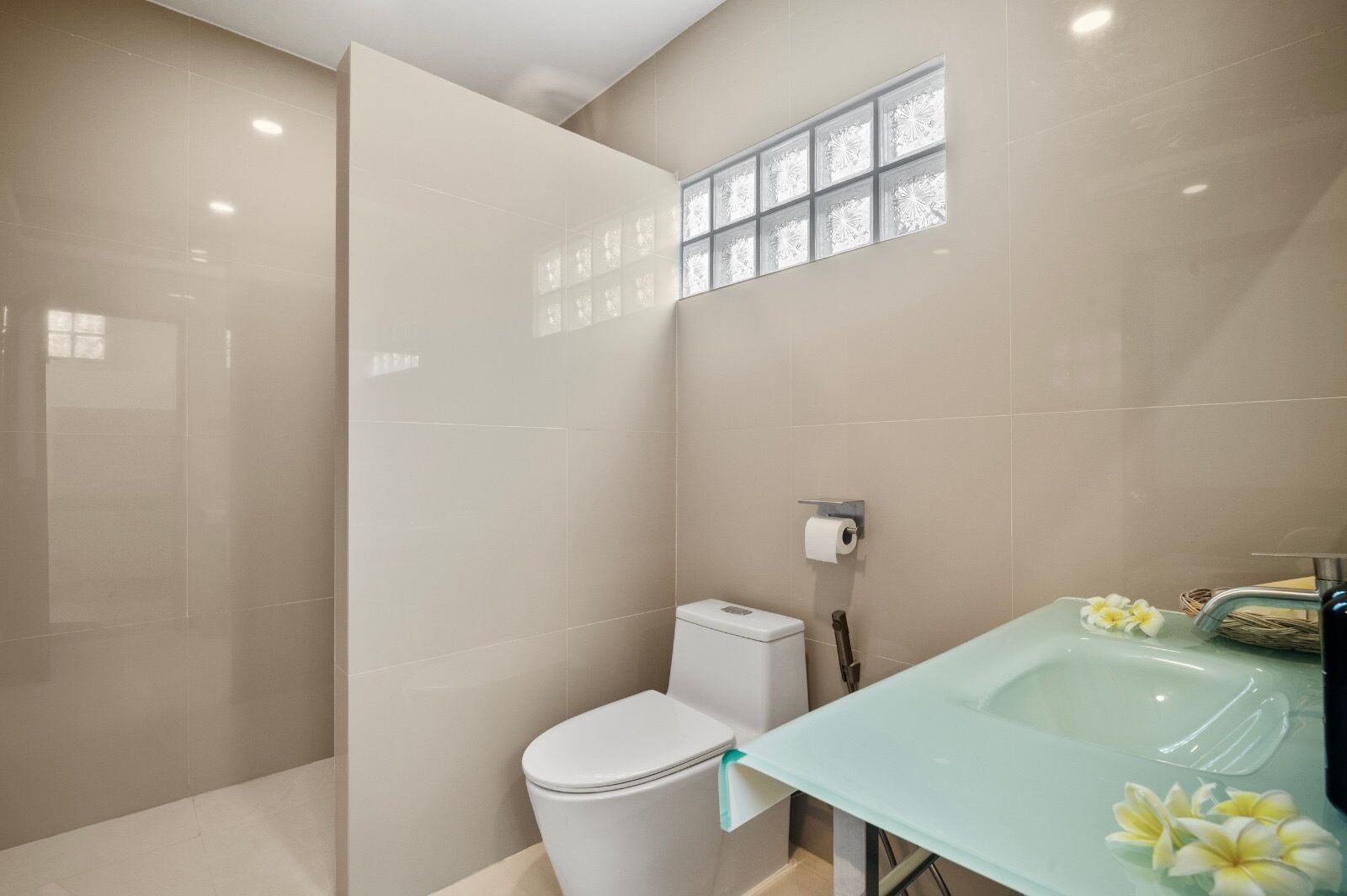 A modern bathroom with a glass shower enclosure, a toilet, and a sink with a decorative flower arrangement.