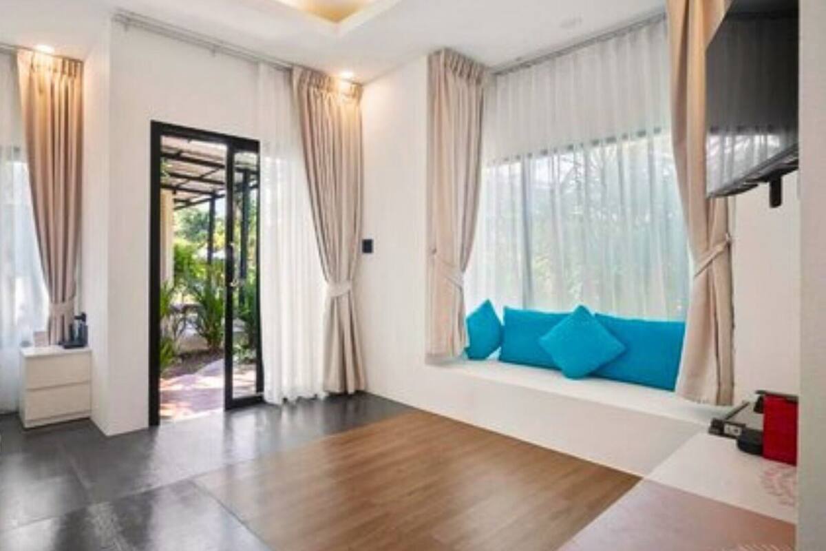 A hotel room with a bed, a window with blue cushions, a door leading outside, and a view of greenery.