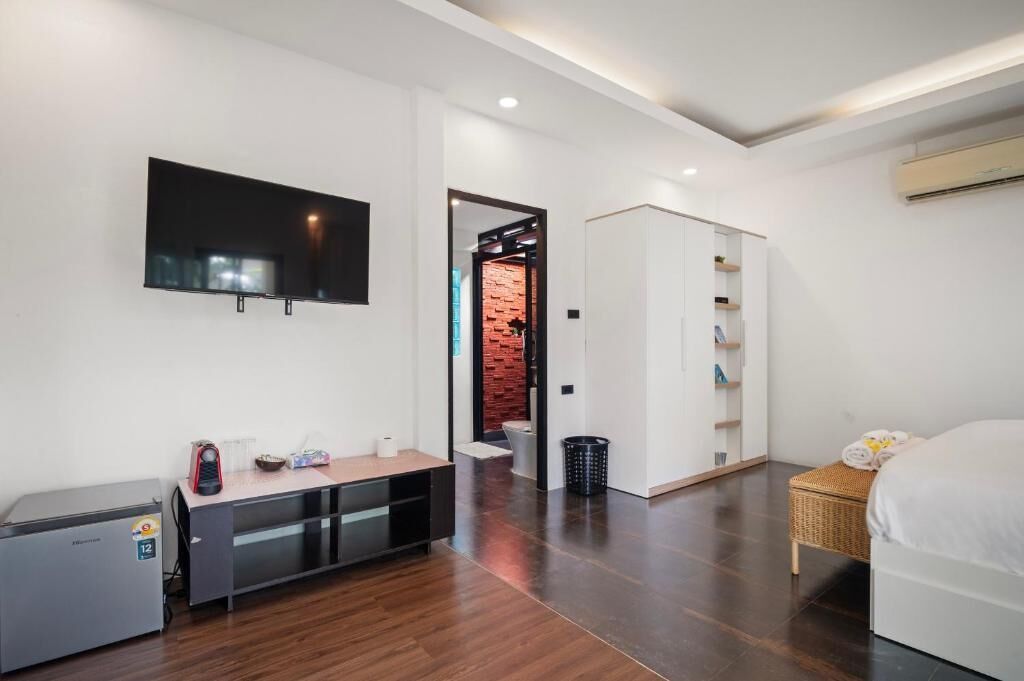 Une chambre d’hôtel moderne équipée d’un téléviseur à écran plat, d’un bureau avec une imprimante, d’une armoire, d’un lit et d’une petite poubelle.