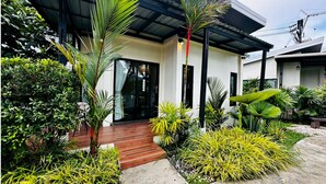 Une maison moderne dotée d’un patio couvert, entourée d’une végétation luxuriante et d’une terrasse en bois.