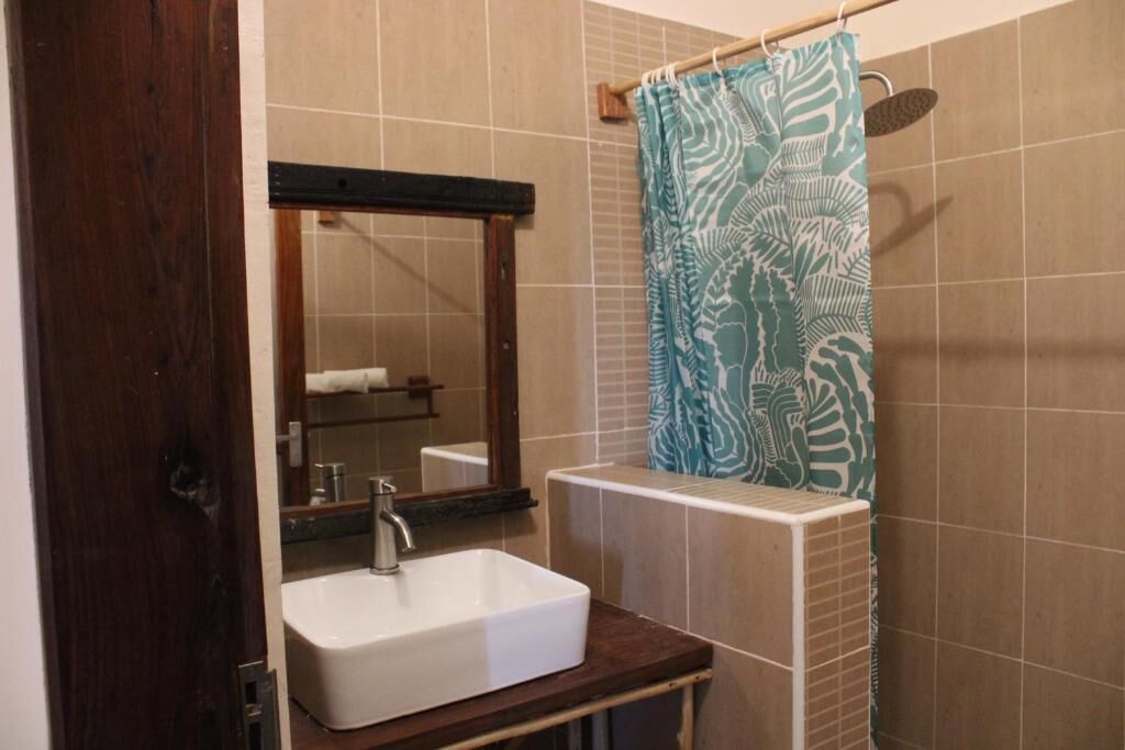 Een badkamer met een wit wastafel, een spiegel en een douchegordijn met bladmotief.
